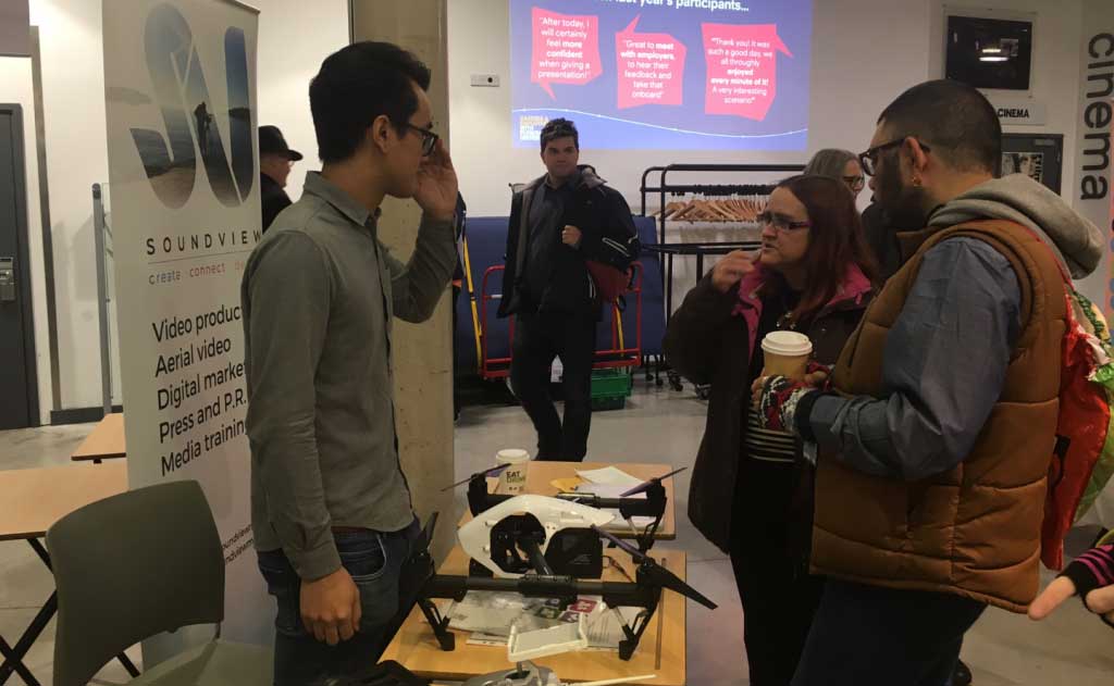 a man stood behind a table with a drone at the Soundview Media business show stall talking to two people