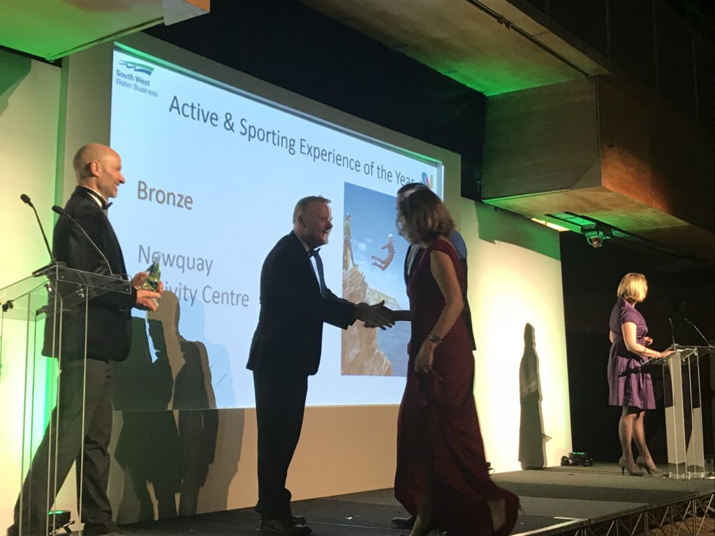 two men present an award to a man and woman whilst shaking their hand