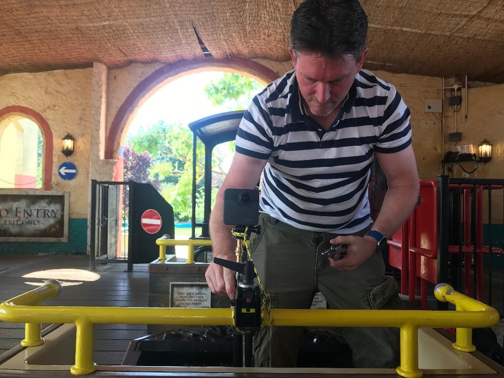 a man on a stationary roller coaster setting up a camera attached to the ride