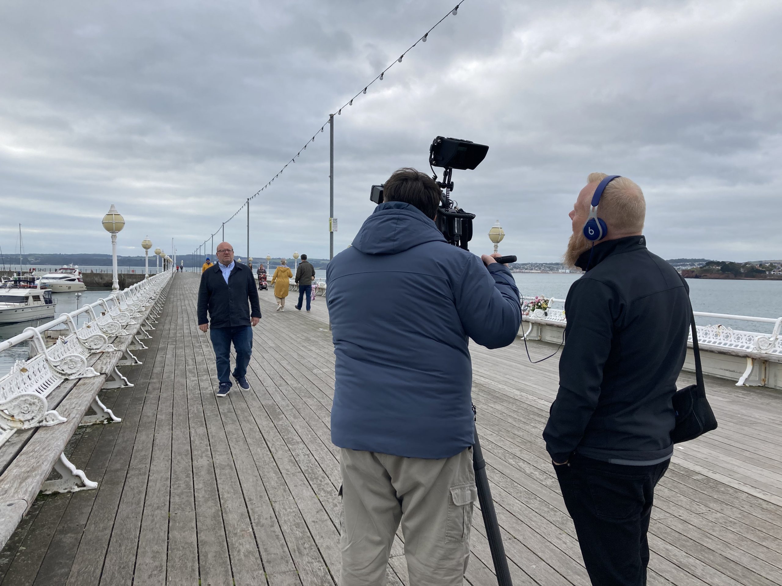 two men filming a male walking down a pier