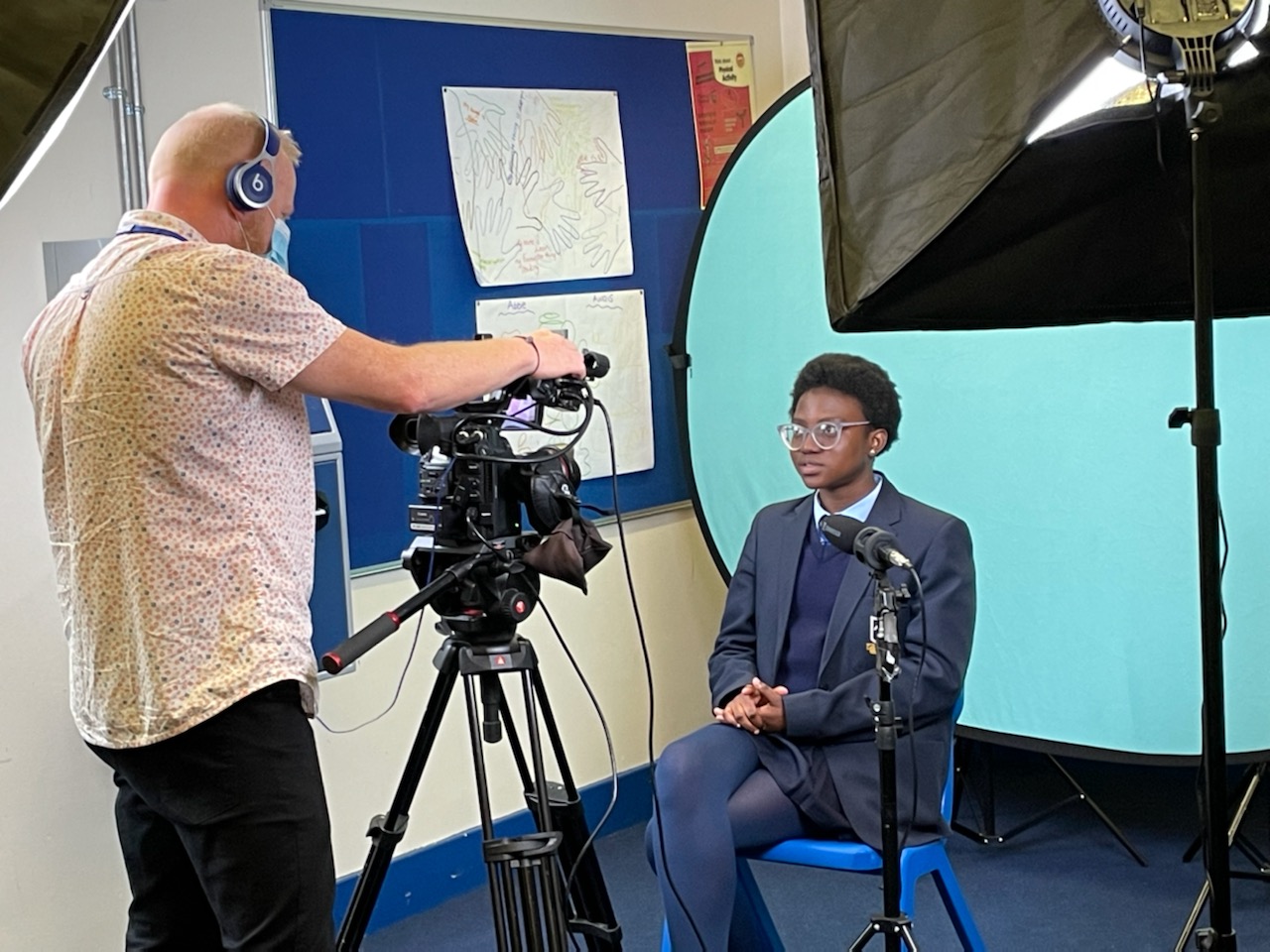 a camera man shooting a school student in front of a blue background in a classroom