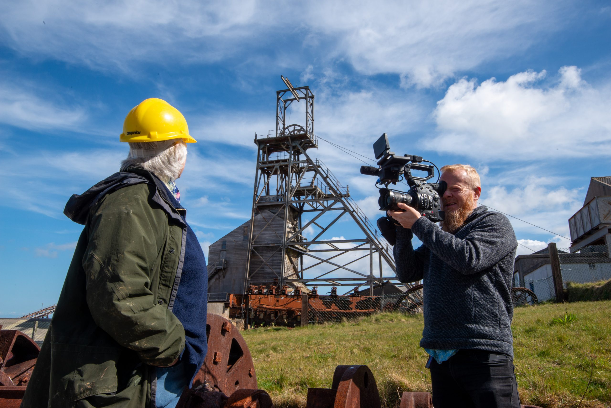 A man filming a woman overlooking Geevor Tin Mine
