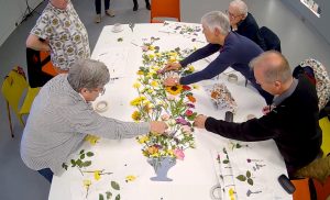 Five people leant over a table covered in dried flowers