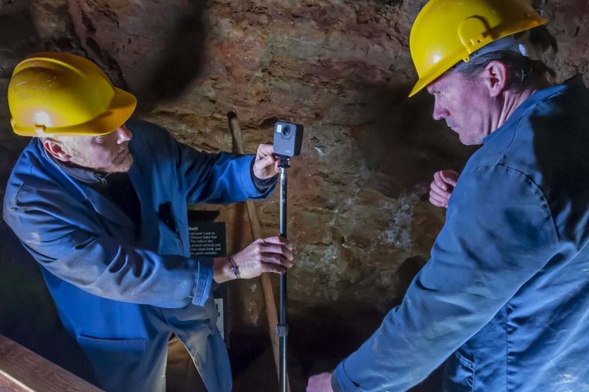 two men staring intently at a time-lapse camera in a mine wearing PPE