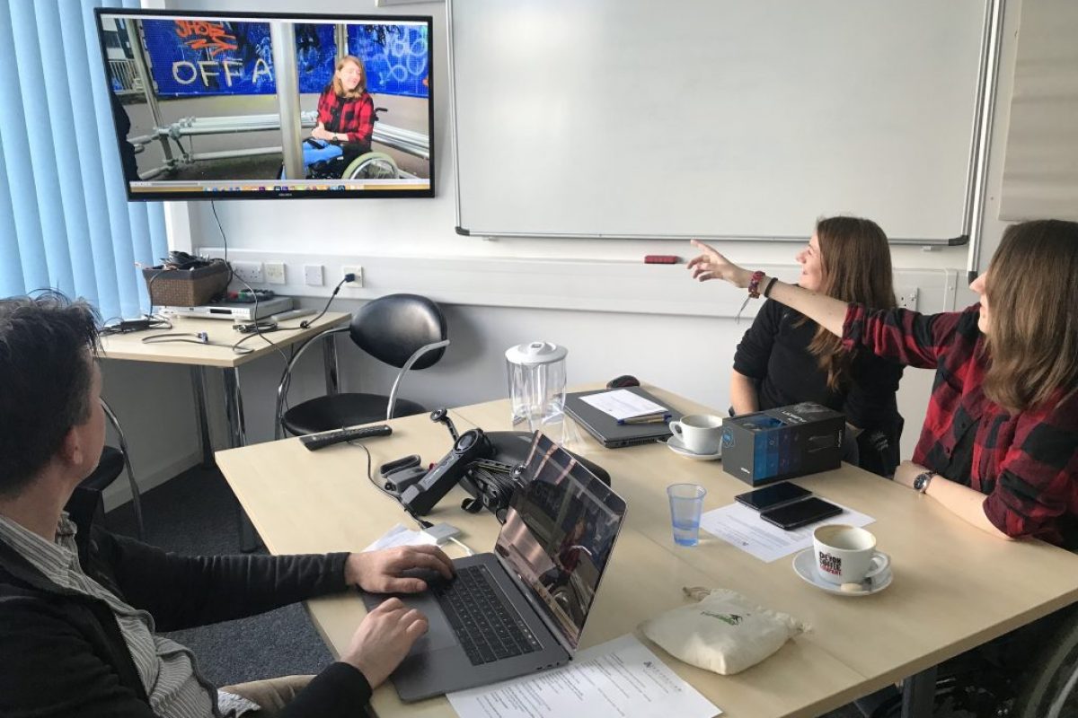 three round a table watching and interacting with a tv