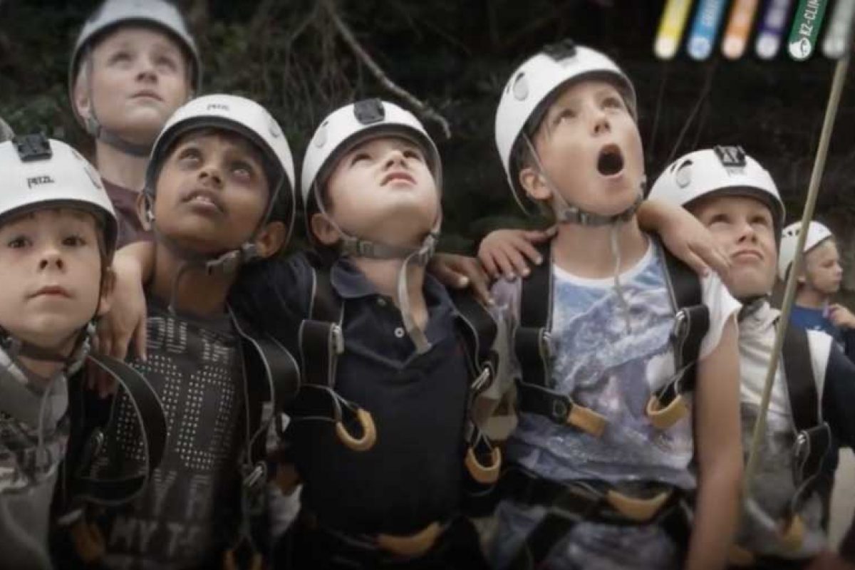 children looking up towards the sky in hard hat helmets and climbing equipment