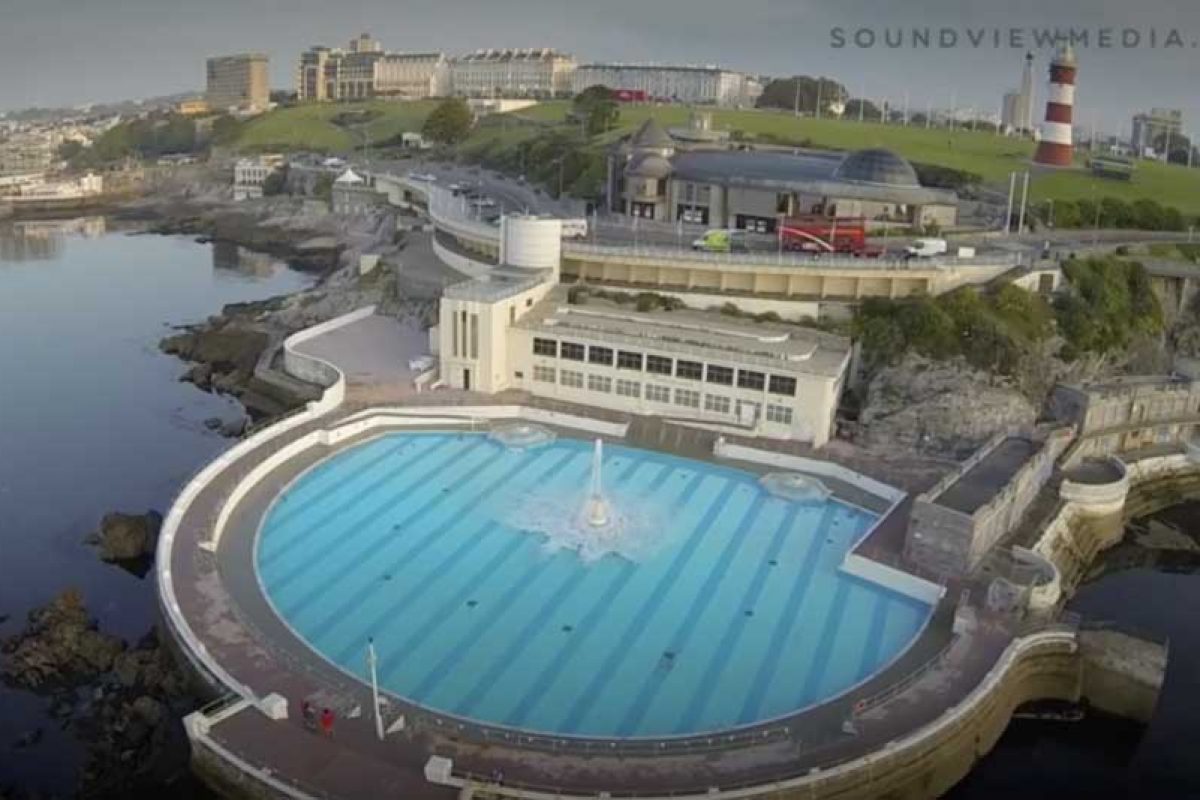 Plymouth lido, an outdoor pool on the barbican with a lighthouse and various other buildings in the background.