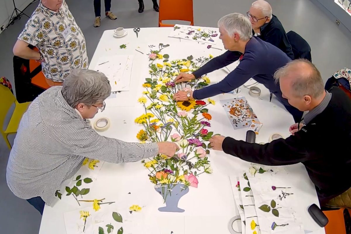 Five people leant over a table covered in dried flowers