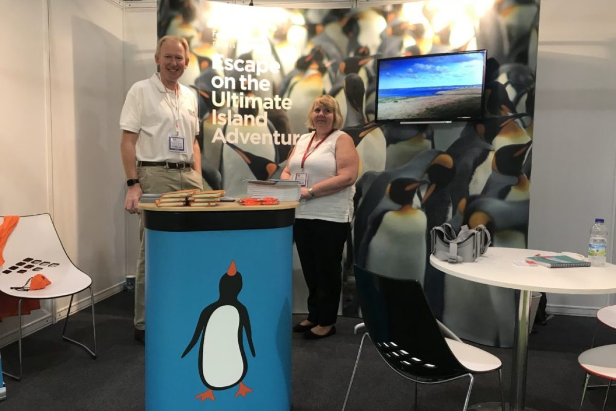 a man and woman posing in front a a business show setup with penguins on the background and podium