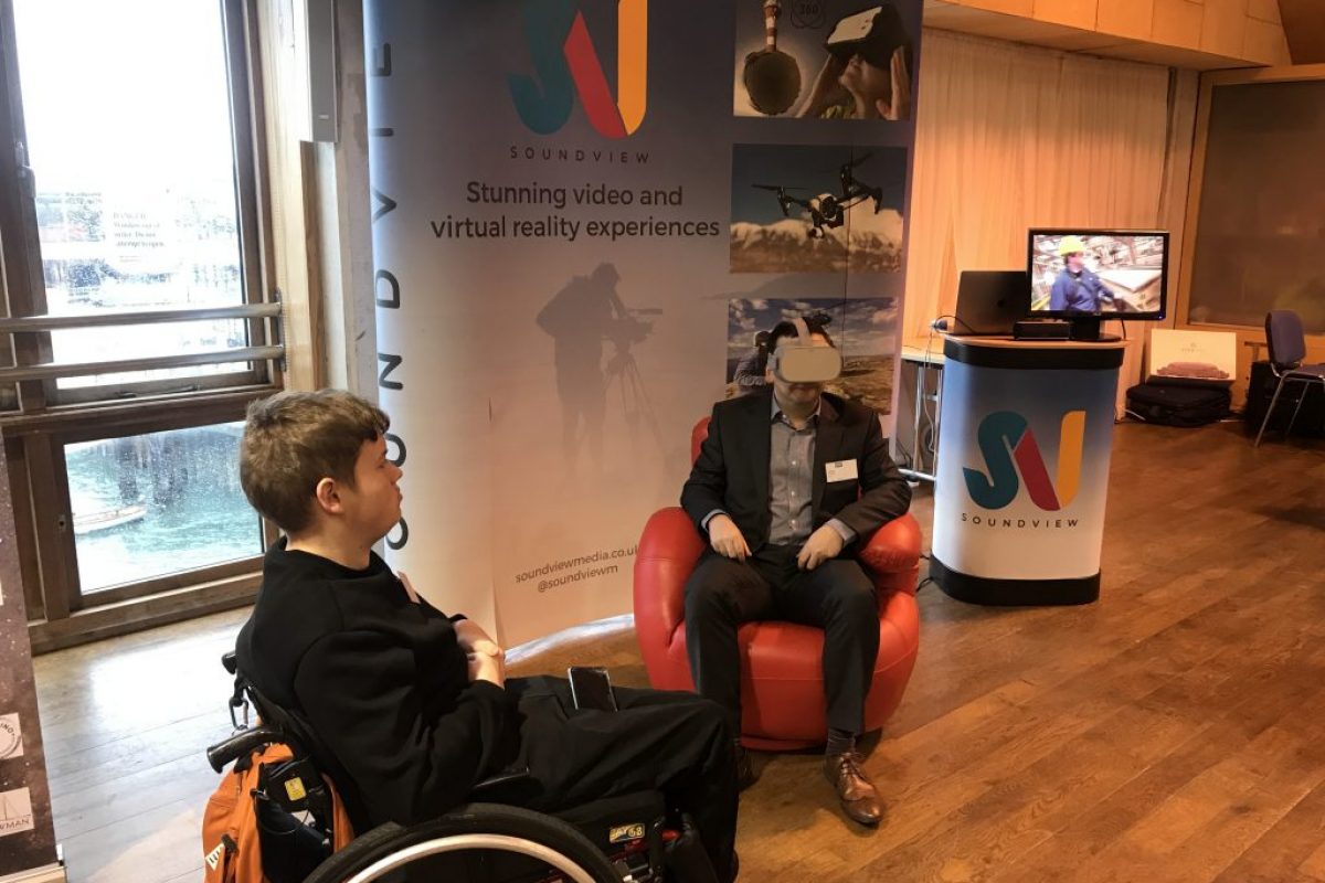 a man in a chair with a VR headset on ands another in a wheelchair watching