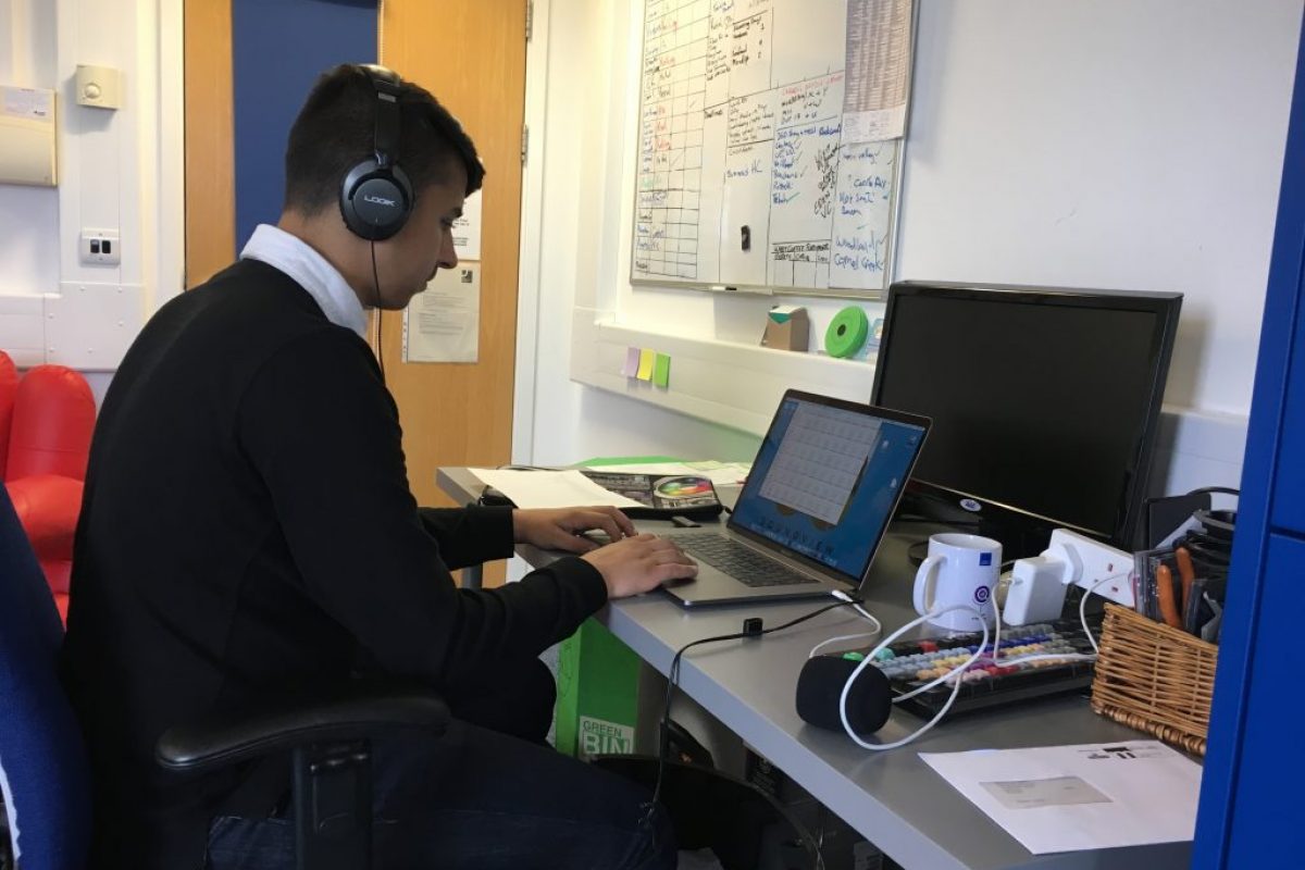 A student sat working on a laptop on a desk in an office room